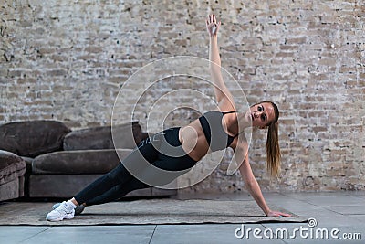 Sporty Caucasian girl doing side plank star exercise working abs and oblique muscles indoors against brick wall Stock Photo