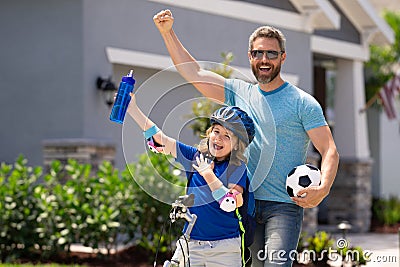 Sporty family. Excited father and son with winning gesture. Father helping son to ride a bicycle. Little kid boy in Stock Photo