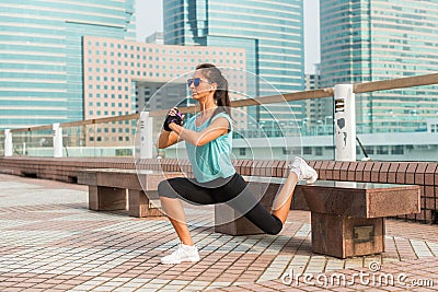 Sporty female athlete doing single leg lunge exercise on bench. Fit young woman working out outdoors in city alley Stock Photo