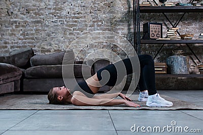 Sporty girl doing floor hip raise or lift exercise lying on floor in her loft apartment Stock Photo