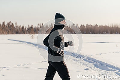 sporty man in sportswear running in a winter park, copy space. a runner trains outdoors, jogging in nature. concept of Stock Photo