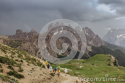 Sporty people in raincoats hiking in Dolomites,Italy.Rainy day outdoors. View of mountain landscape with dark moody Stock Photo