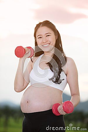 Sporty pregnant asian woman exercising with dumbbells Stock Photo