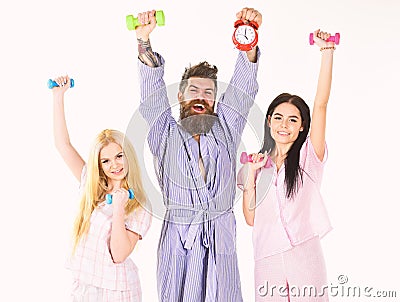 Sporty regime concept. Man in robe, trainer holds clock, attractive young women in pajamas doing exercises with Stock Photo