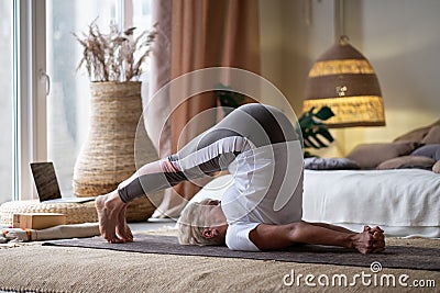 Sporty senior woman doing halasana, plough pose or yin yoga snail posture Stock Photo