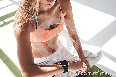 Sporty sunburn woman sitting on yoga mat and using smartwatch for checks results in fitness app Stock Photo
