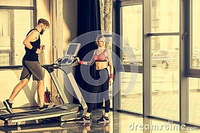 Sporty woman standing near bearded sportsman training on treadmill Stock Photo