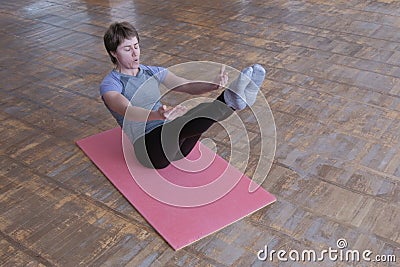 Sporty woman in traditional yoga pose. Fitness exercise to strengthen the abdominal muscles. A girl in a gray t-shirt sitting on a Stock Photo