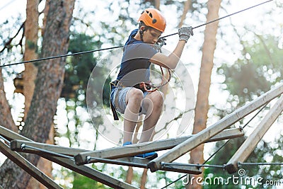 Sporty, young, cute boy in white t shirt spends his time in adventure rope park in helmet and safe equipment in the park Stock Photo