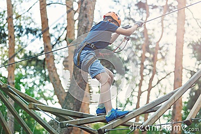 Sporty, young, cute boy in white t shirt spends his time in adventure rope park in helmet and safe equipment in the park Stock Photo