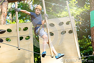 Sporty, young, cute boy in white t shirt spends his time in adventure rope park in helmet and safe equipment in the park Stock Photo