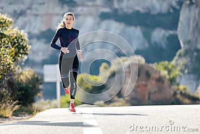 Sporty young woman running on mountain road in beautiful nature Stock Photo