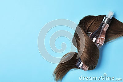 Spray bottle wrapped in lock of hair on blue background, flat lay with space for text. Natural cosmetic products Stock Photo