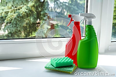 Spray bottles of detergents and sponges on window sill indoors, space for text. Cleaning supplies Stock Photo