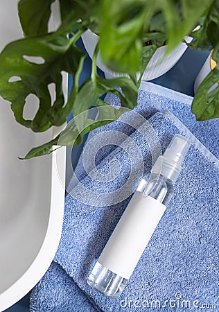 Spray cosmetic bottle on blue towels near basin and green monstera in bathroom, mockup Stock Photo