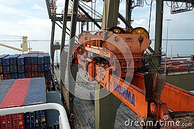 Spreader of gantry cranes operated by stevedores in close view is moving to loaded ship with cranes. Editorial Stock Photo
