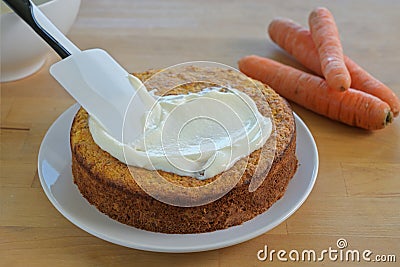 Spreading frosting on a freshly baked carrot cake, wooden table Stock Photo