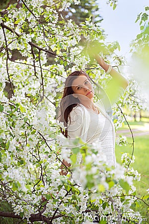 Spring brunette girl standing outdoor in blooming trees. Beautiful romantic woman in apple flowers. Young woman enjoying nature. Stock Photo