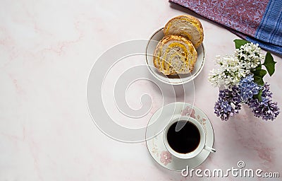 Cup of coffee, lilac flowers Syringa vulgaris and a sweet homemade turmeric bun on a pastel pink marble background. Stock Photo