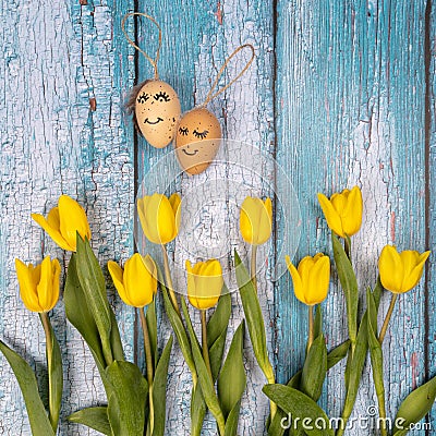 Spring composition of yellow flowers and eggs with a painted cute face on a blue background. Congratulations on Easter Stock Photo