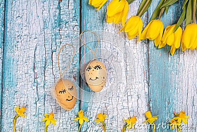 Spring composition of yellow flowers and eggs with a painted cute face on a blue background. Congratulations on Easter. Stock Photo