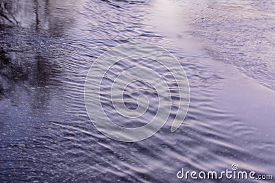 Spring creek flows through the asphalt road. Early spring Stock Photo