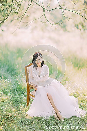 Spring field composition of the woman in the long white dress sitting in the old modern chair. Stock Photo