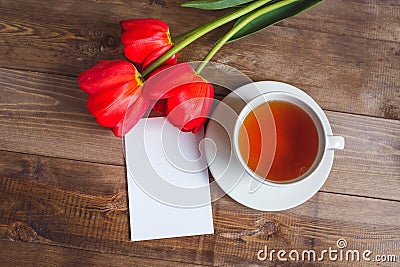 Spring flowers. Bouquet of Red tulips with tea cup and present card on brown wooden background. Mother`s Day and Stock Photo