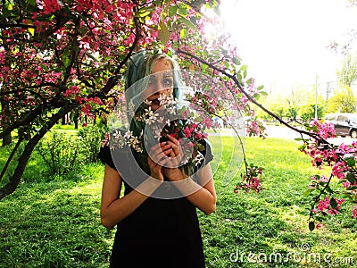 Spring girl with green hair stands under blooming cherry tree, which blooms Stock Photo