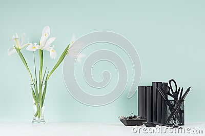 Spring green mint menthe interior of office with black stationery, books, fresh white iris bouquet in transparent glass vase. Stock Photo
