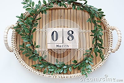 Spring green wreath of leaves rests on wooden bamboo tray. Boxwood wreath. Flat lay, top view. Wooden block calendar 8 March. Conc Stock Photo
