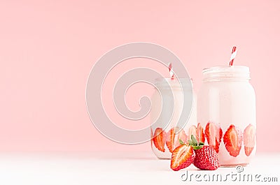 Spring healthy milk beverages with cut ripe strawberry, red striped straws on gentle pastel pink background, white wood table. Stock Photo