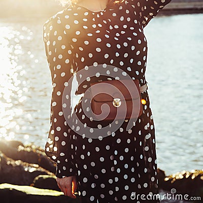 Spring summer casual female outfit with long black dress in polka dots with leather brow purse belt bag Stock Photo