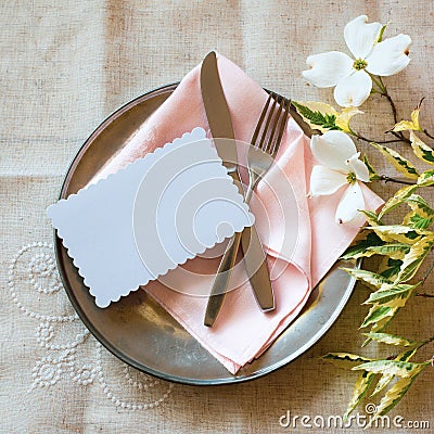 Spring Table Place Setting with white flowers, pink napkin, silverware and a blank card for party menu or invitation. Stock Photo