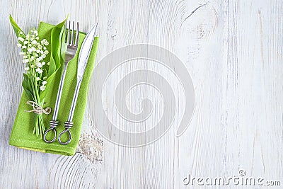 Spring table setting: bouquet of the lilies of the valley and cutlery on the green napkin on white wooden background Stock Photo