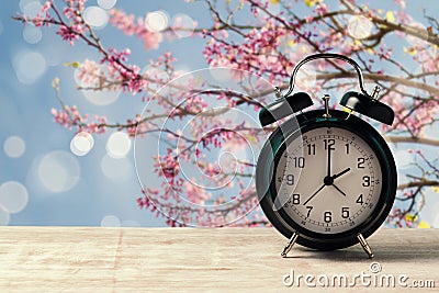 Spring time change concept with alarm clock on wooden table over nature tree blossom Stock Photo