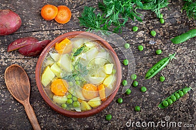 Spring vegetable broth with peas, young potatoes and carrots served in a clay bowl Stock Photo