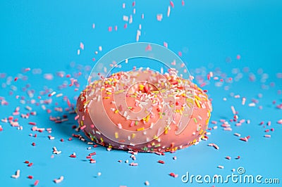 Sprinkles falling from top on Tasty pink strawberry donut. Delicious dessert on blue background. Stock Photo