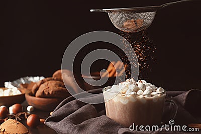 Sprinkling of hot drink with cacao powder on dark background Stock Photo