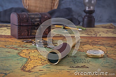 Spyglass and a compass lie on an old map against the background of a forged chest with coins. Stock Photo