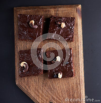 Square baked slices of brownie chocolate cake with walnuts on a brown wooden surface. Cooked homemade food. Chocolate pastry Stock Photo