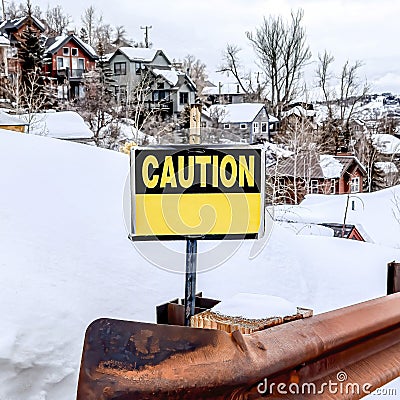 Square Caution sign on the rusty guardrail of a road in the snowy mountain in winter Stock Photo