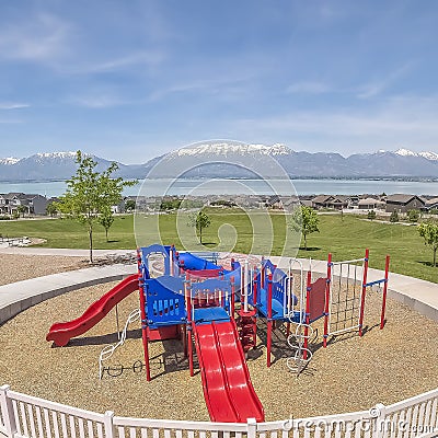Square frame Childrens playground ovelooking homes lake and snow peaked mountain under sky Stock Photo