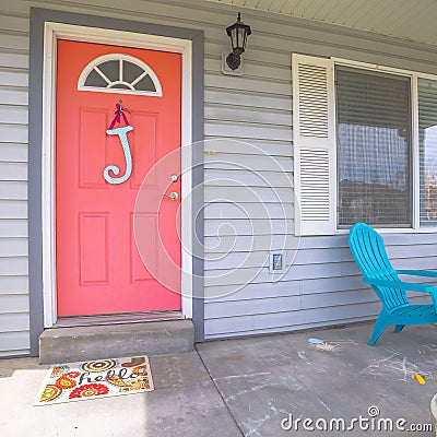 Square frame Red front door of house with blue porch chairs against windows with shutters Stock Photo