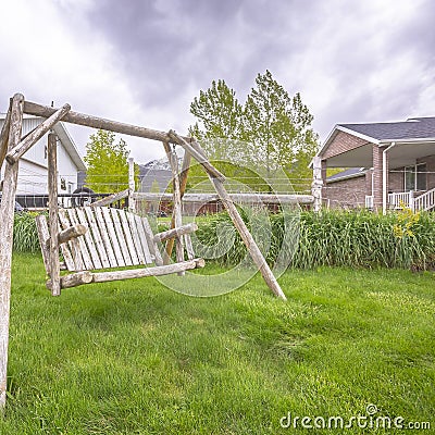 Square frame Wooden bench swing at the lush grassy yard of a home with white picket fence Stock Photo