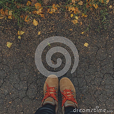 square image feet in brown boots on the cracked ground with yellow fallen leaves. Autumn background. lifestyle concept. Stock Photo