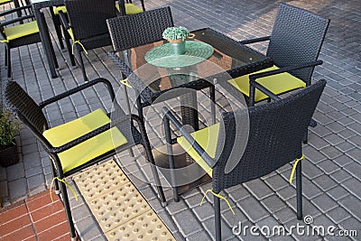 Square table with green decorative round cloth and flowers and four black wicker chairs with yellow padded cushions Stock Photo