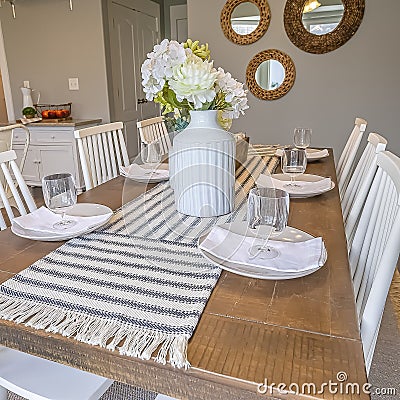 Square Table runner flowers glasses napkins and plates arranged on top of dining table Stock Photo