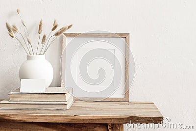 Square wooden frame mockup on vintage bench, table. Modern white ceramic vase with dry Lagurus ovatus grass, books and Stock Photo