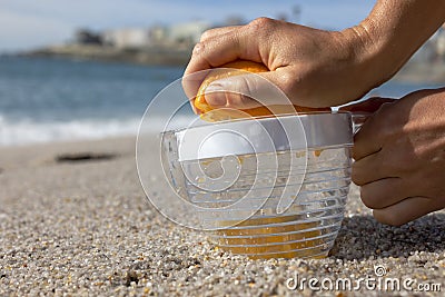 Squeezing an orange against the backdrop of the ocean. Stock Photo